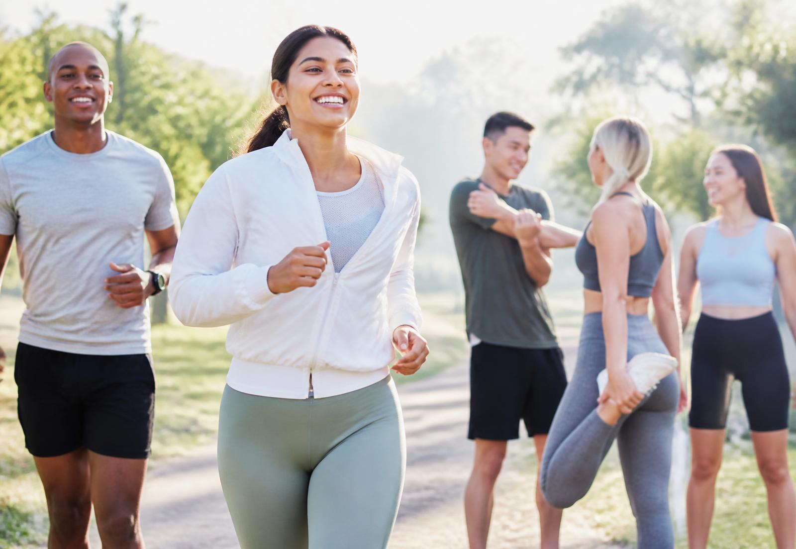 Adults jogging and stretching outdoors on a sunlit park trail